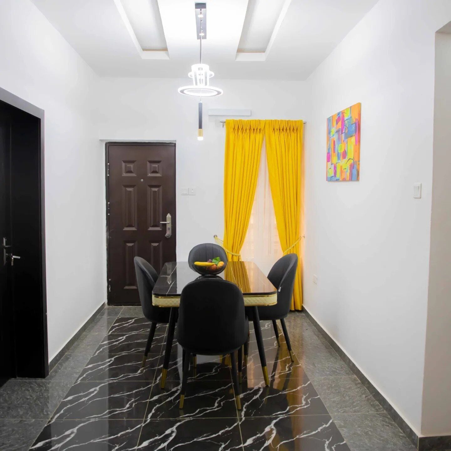 A dining area with a black marble floor, a dark wooden door, and a table with chairs.