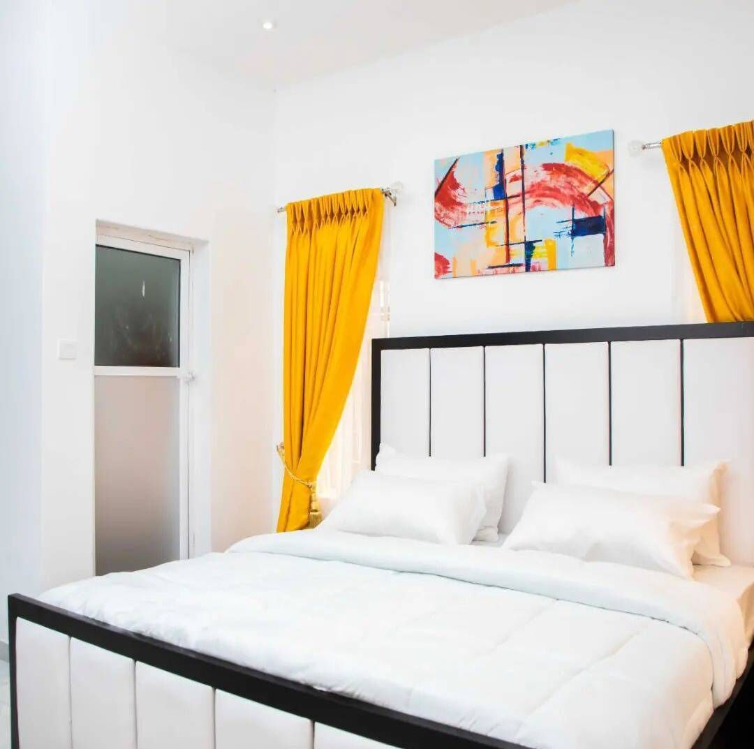 Een slaapkamer met een bed, witte gordijnen en een kleurrijk abstract schilderij aan de muur.