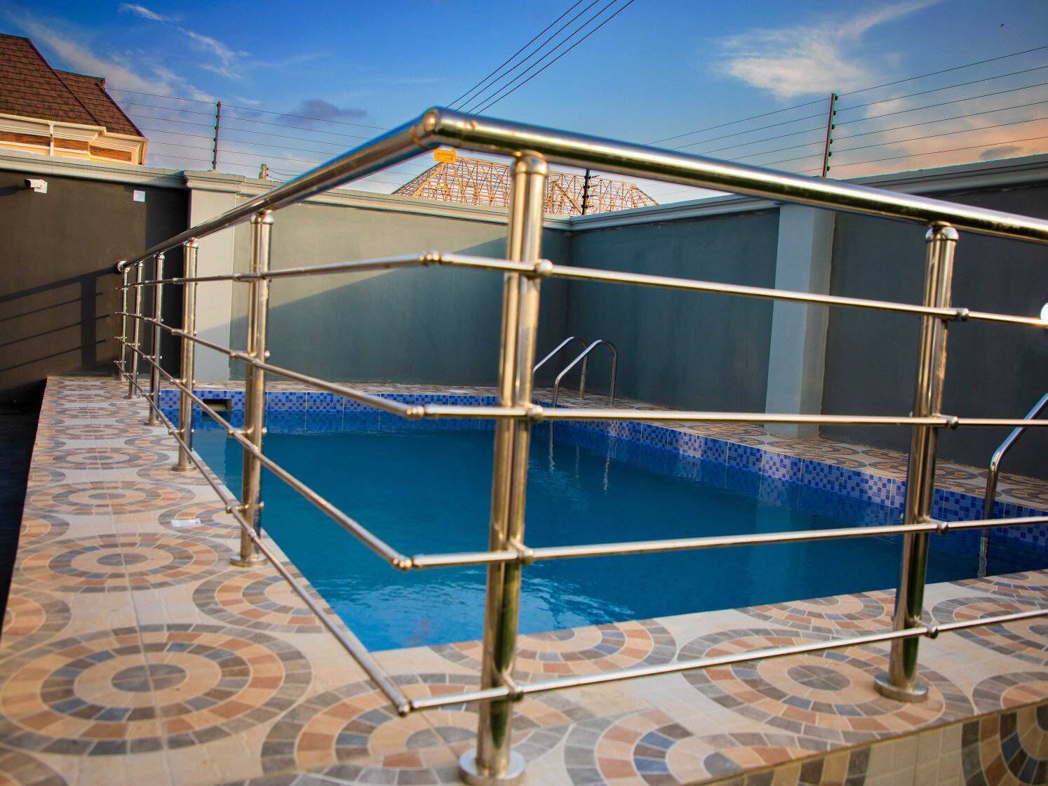 A swimming pool with a metal safety railing, surrounded by a tiled deck with a circular pattern.