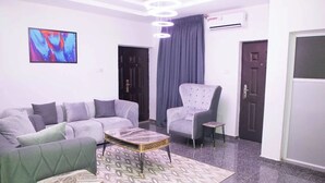 A modern living room with a grey sofa, a matching armchair, and a coffee table. There is a painting on the wall and a ceiling light fixture. - Delight Hotel and Suites Ado Ekiti (Ado Ekiti)