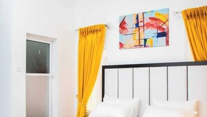 A bedroom with a bed, white curtains, and a colorful abstract painting on the wall. - Delight Hotel and Suites Ado Ekiti (Ado Ekiti)