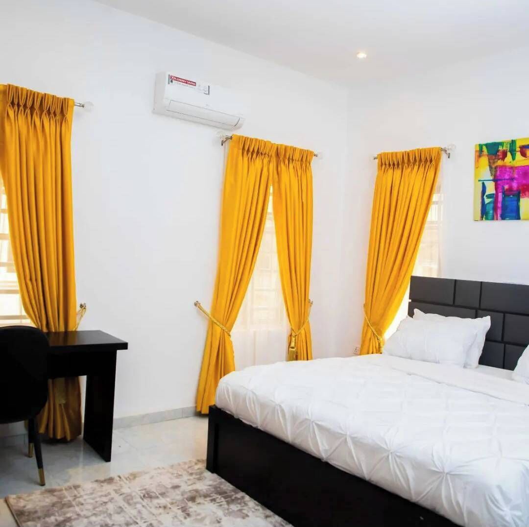 Una habitación de hotel con una cama, un escritorio y dos ventanas con cortinas amarillas.