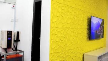 A room with a yellow textured wall, a mounted TV, a white cabinet, and a metal cart with drawers.