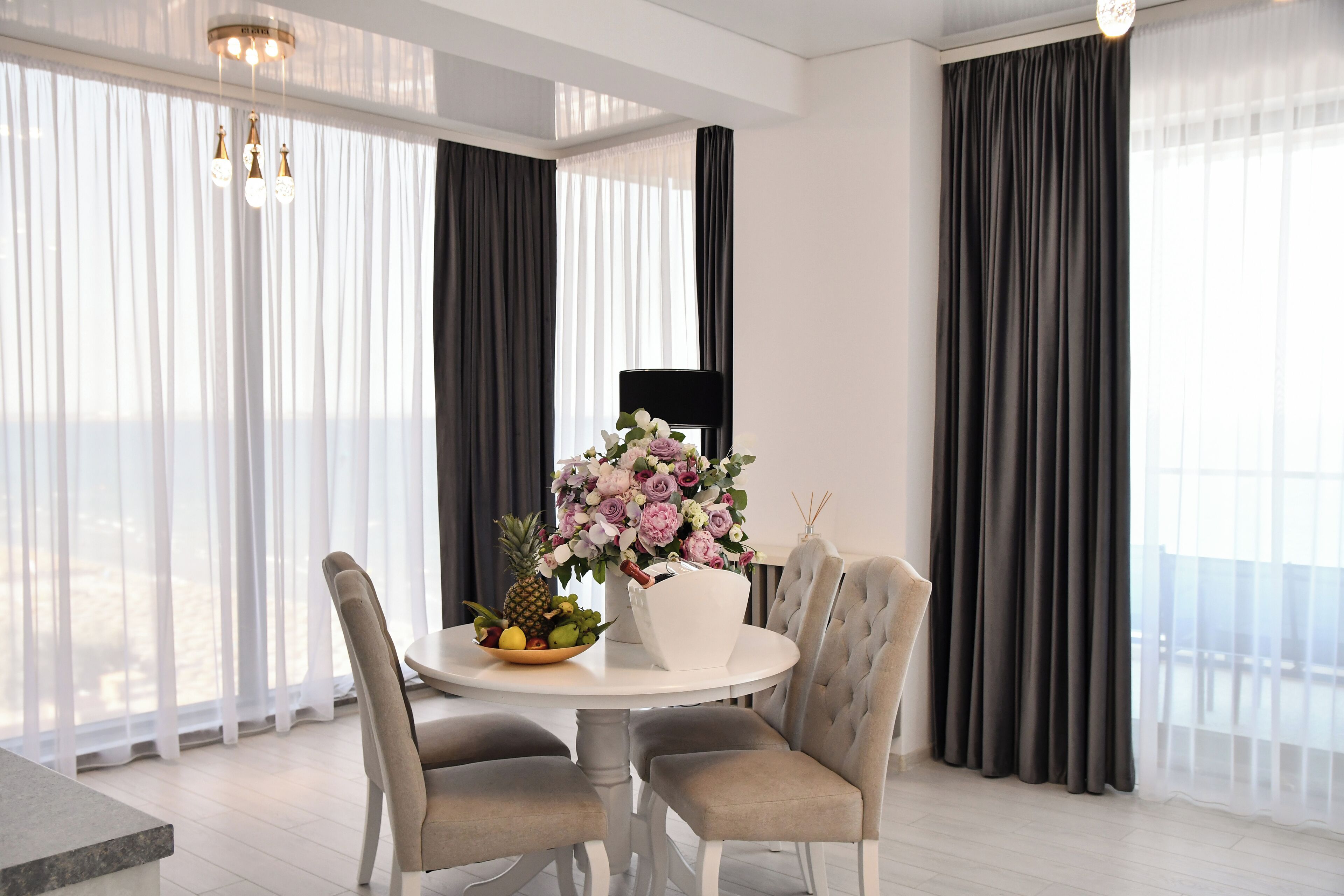 A dining area with a round table, four chairs, a vase of flowers, and a fruit bowl.