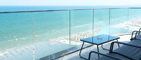 A balcony with a glass railing overlooking a beach with people and umbrellas.