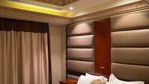Hotelkamer met een groot bed, een houten nachtkastje, een hoofdbord met een structuurpatroon en een decoratief plafond.