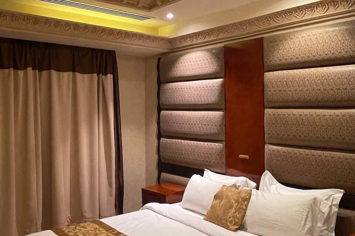 A hotel room with a large bed, a wooden nightstand, a headboard with a textured pattern, and a decorative ceiling.