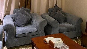 Een kamer met twee grijze banken, een houten salontafel en een groot raam met gordijnen.