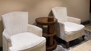 Een hotel lobby met twee fauteuils, een klein houten tafeltje en een schilderij van bomen aan de muur.