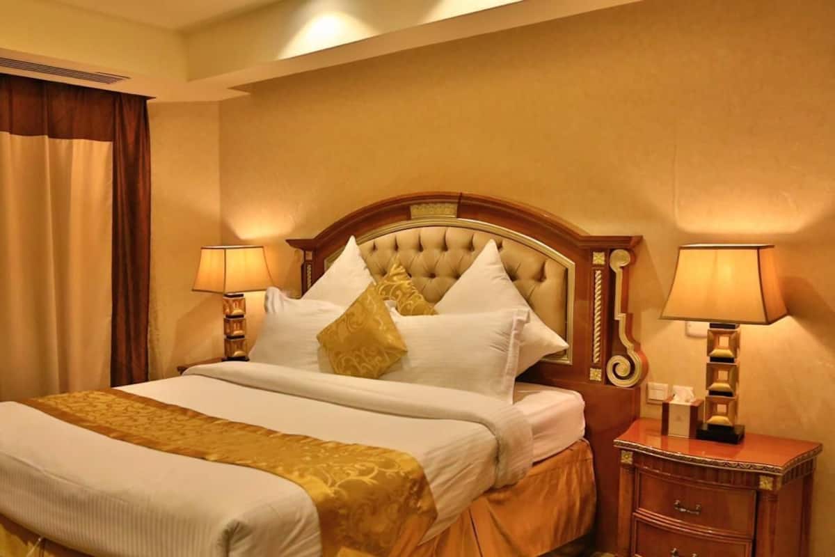 A hotel room with a large bed, two bedside lamps, a wooden nightstand, and a headboard with a tufted design.