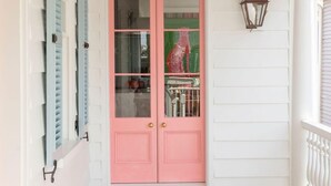 A white porch with a pink door, wooden floor, and a lantern. - Casa Zoë | Royal House – Charleston’s Crown (Charleston)