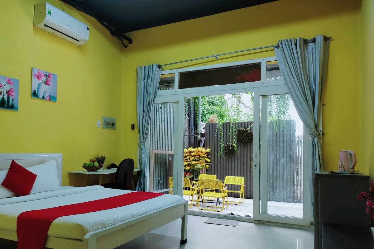Une chambre d’hôtel avec un lit, une petite table sur laquelle se trouve un panier, une chaise, et une chaise jaune placée à l’extérieur d’une porte-fenêtre coulissante.