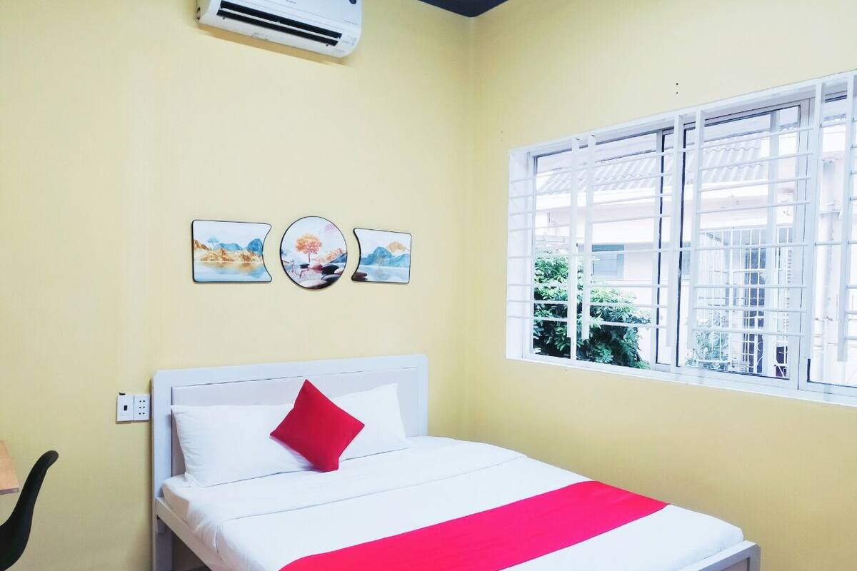 Une chambre d’hôtel avec un lit, une fenêtre avec des stores blancs et trois tableaux accrochés au mur.