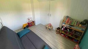 Ein Zimmer mit einer Couch, einer kleinen Spielküche, einem Bücherregal und einem Kleiderschrank.