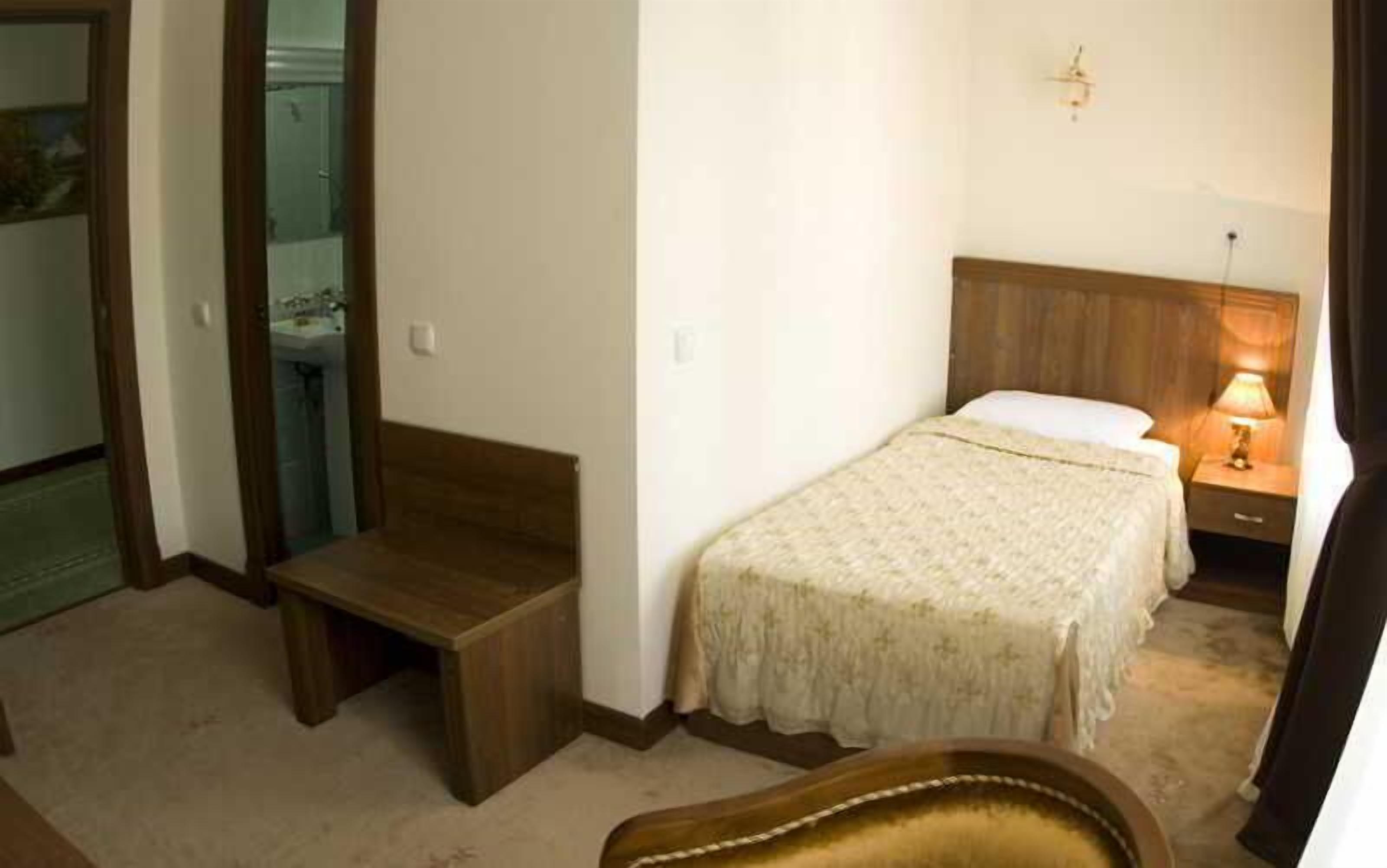 A small bedroom with a single bed, bedside table, nightstand, and a lamp.