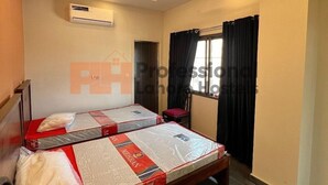 Una habitación de hotel con dos camas, aire acondicionado, ventilador de techo y una ventana con cortinas.