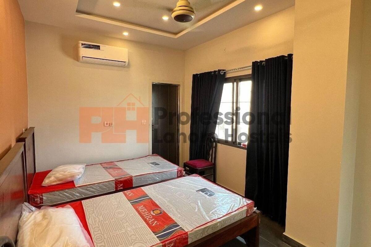 Ein Hotelzimmer mit zwei Betten, einer Klimaanlage, einem Deckenventilator und einem Fenster mit Vorhängen.