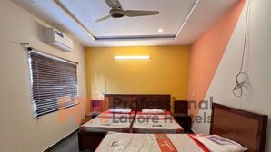 Quarto de hotel com duas camas, um ventilador de teto, um ar condicionado e uma placa com 'Professonal Hotels Lahore'.
