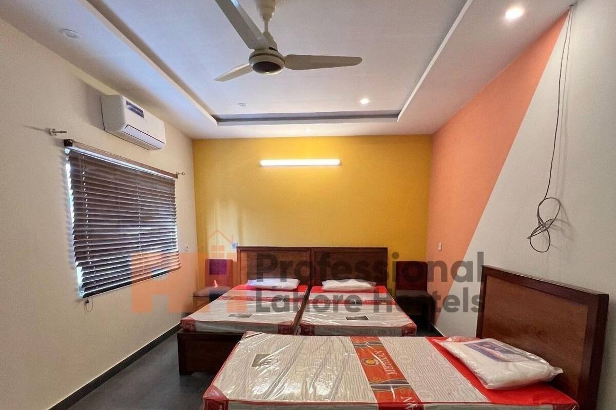 Ein Hotelzimmer mit zwei Betten, einem Deckenventilator, einer Klimaanlage und einem Schild mit der Aufschrift 'Professonal Hotels Lahore'.