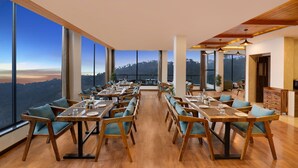 Un espace repas avec des tables et des chaises, de grandes fenêtres et une vue sur les montagnes.