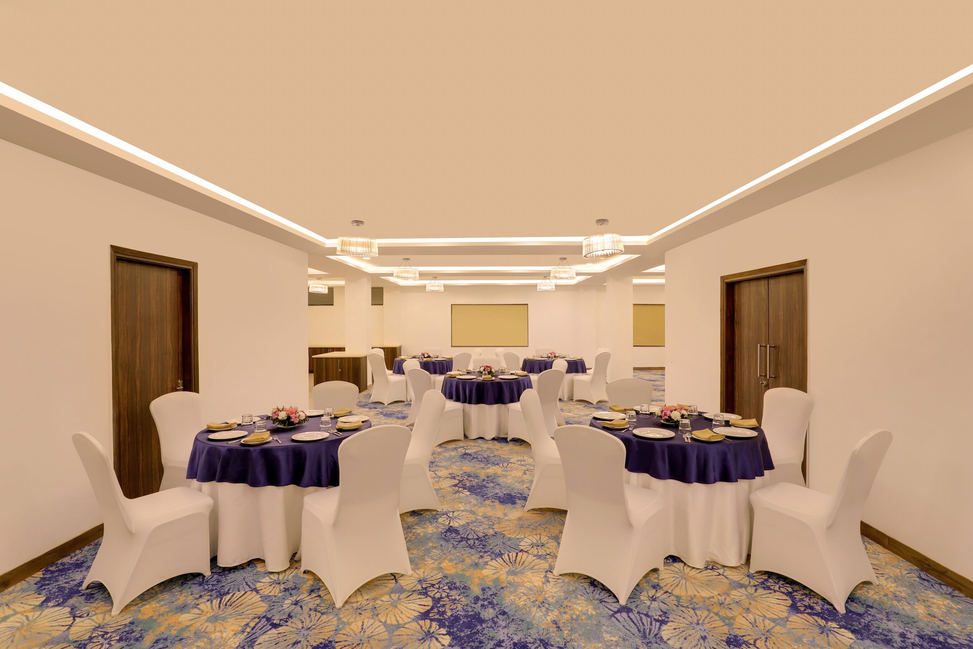 Una sala de conferencias con mesas redondas, sillas blancas y alfombra azul.