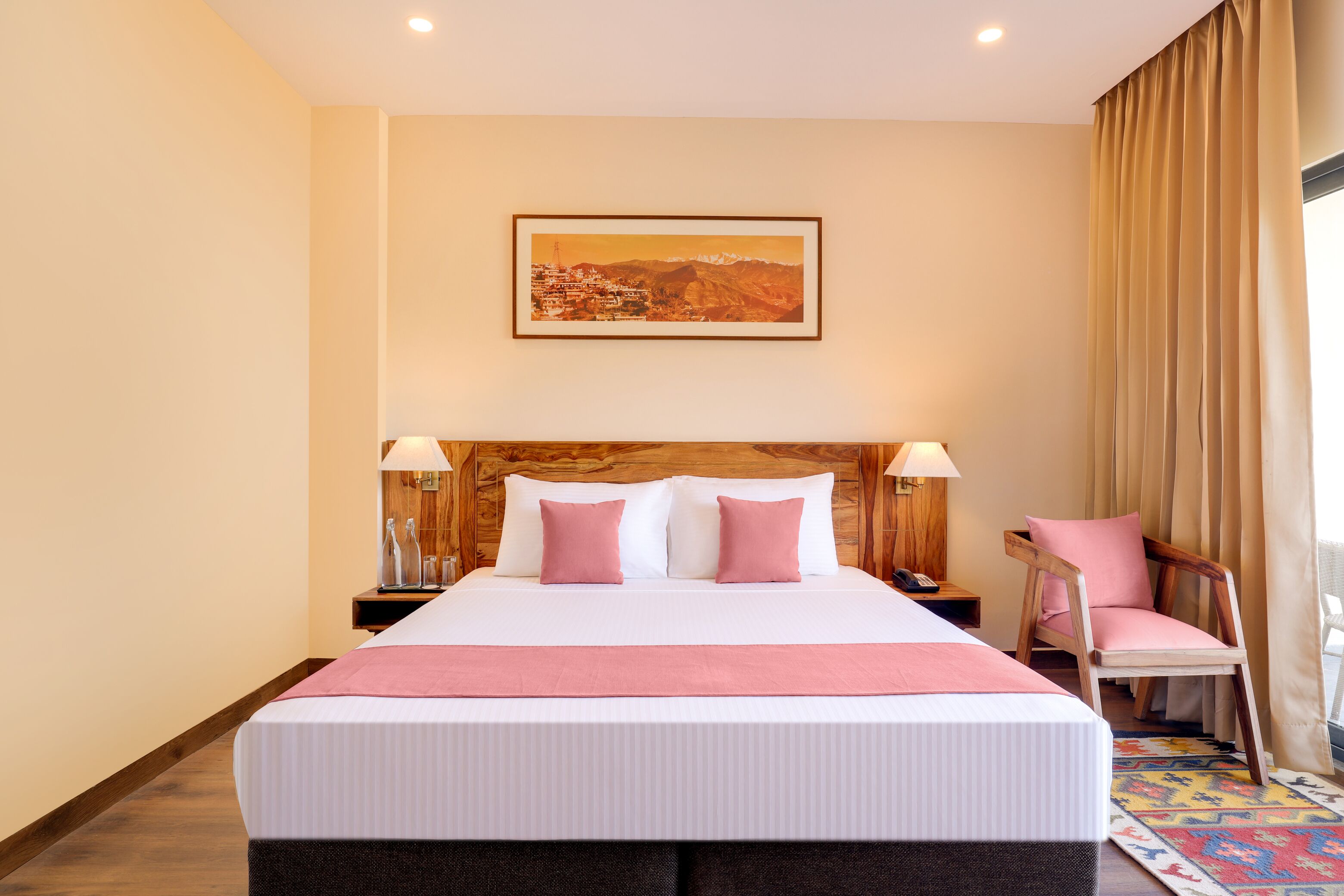 Une chambre d’hôtel avec un grand lit, une tête de lit en bois, deux lampes de chevet, une chaise et un tableau encadré au mur.