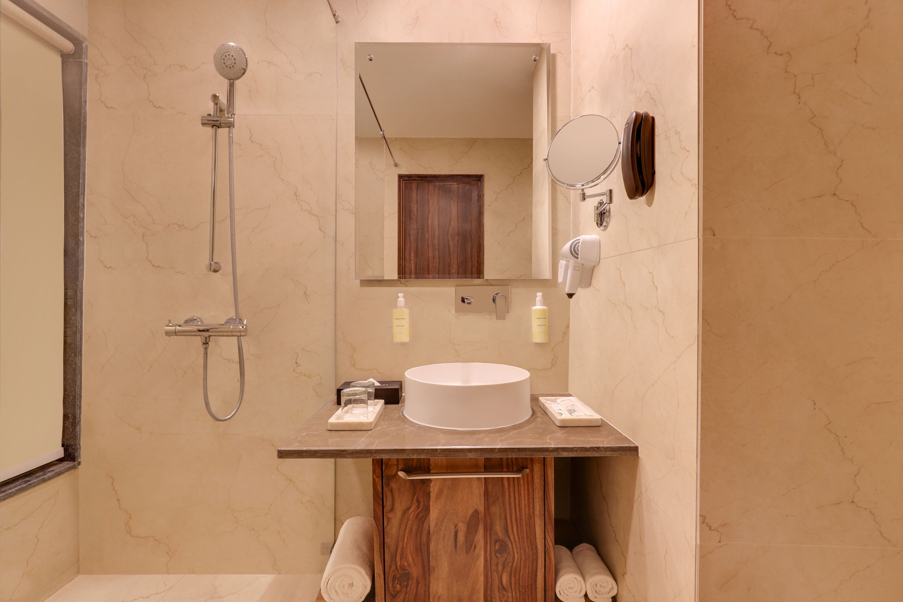 Un bagno moderno con parete in marmo, lavandino tondo, doccetta a mano, specchio e porta asciugamani.