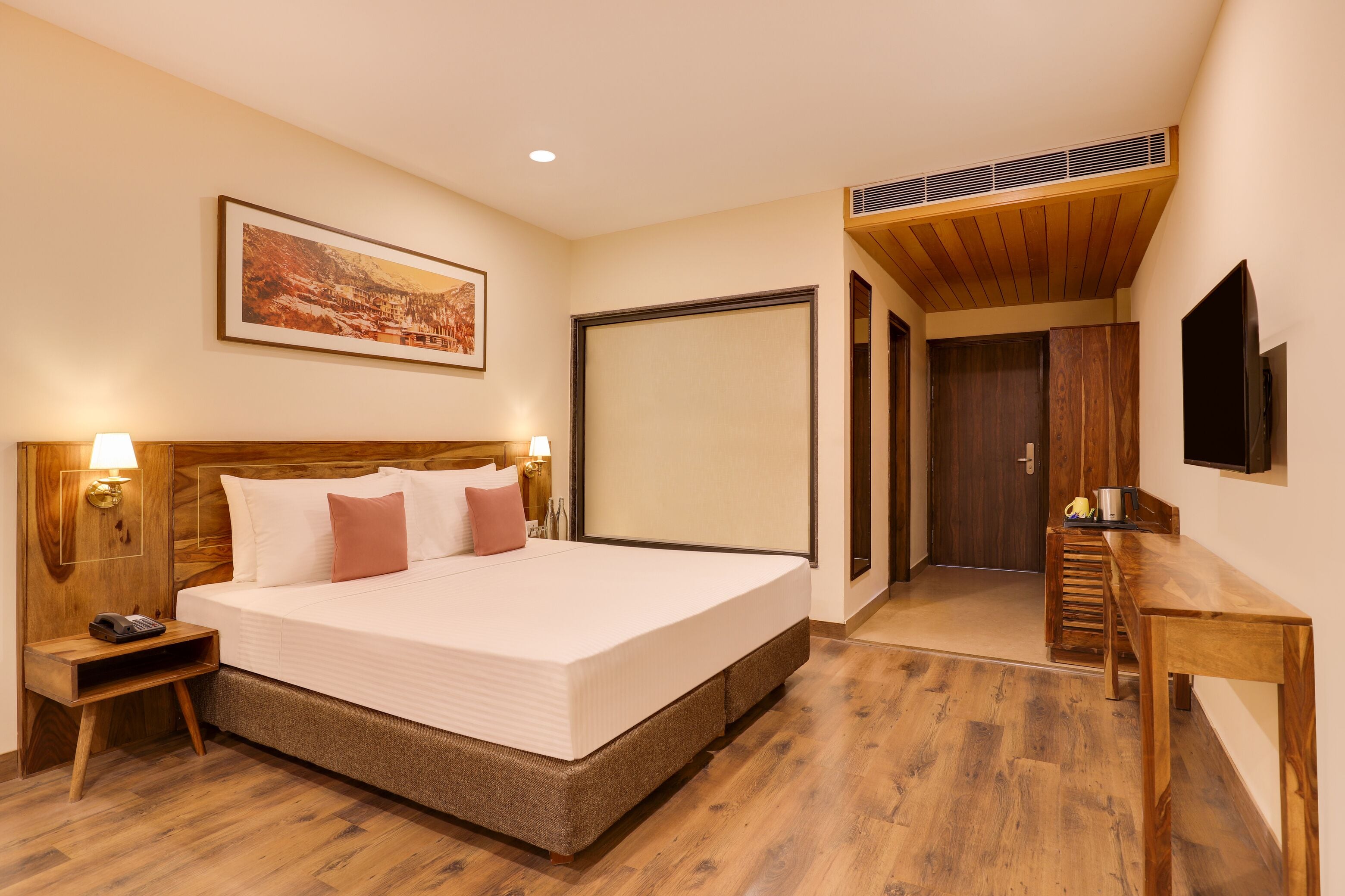 Une chambre d’hôtel avec un grand lit, une tête de lit en bois, des lampes de chevet, un bureau en bois et un téléviseur fixé au mur.