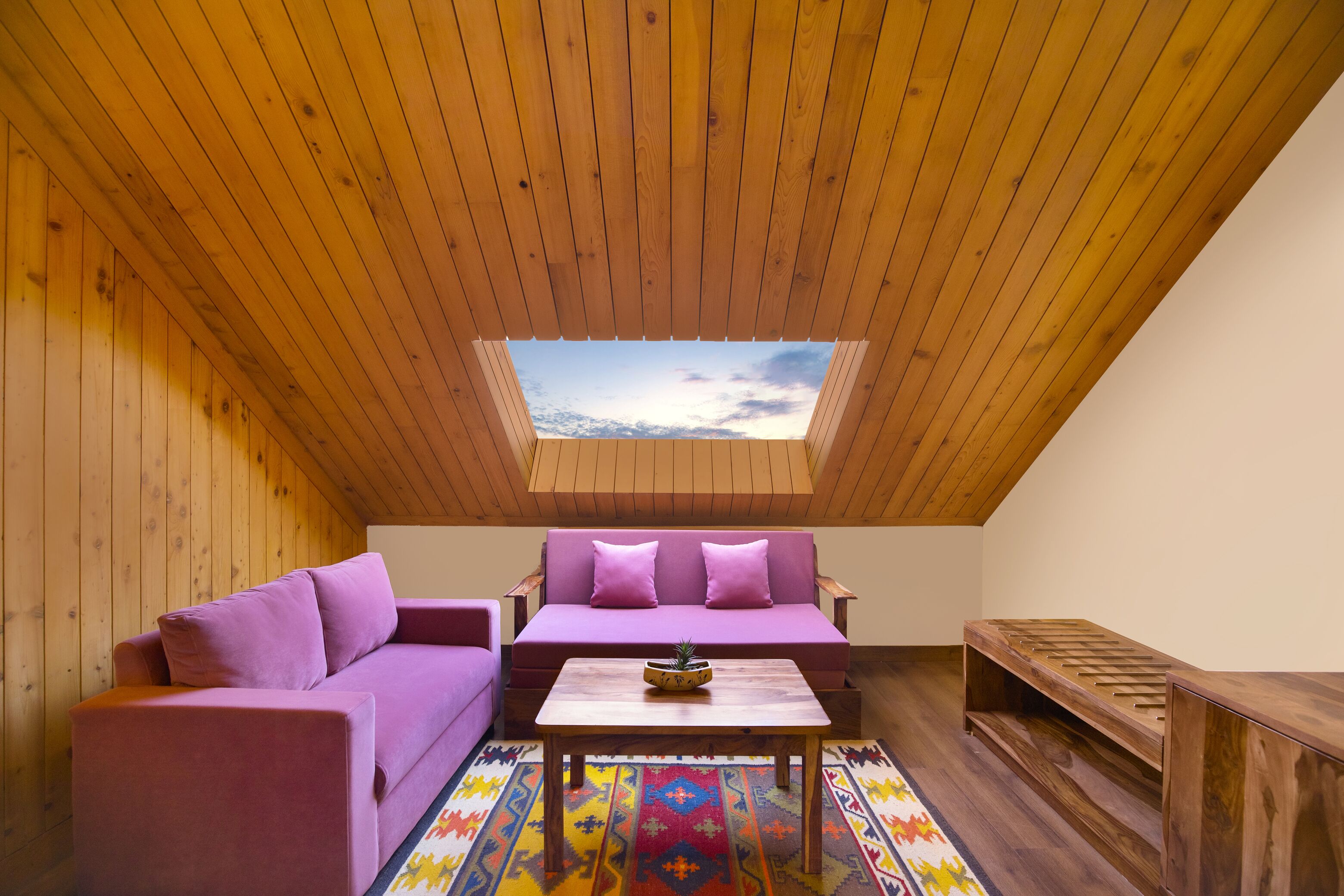 A cozy room with a sloped ceiling, wooden walls, a purple sofa, a matching armchair, a wooden coffee table, and a colorful rug.