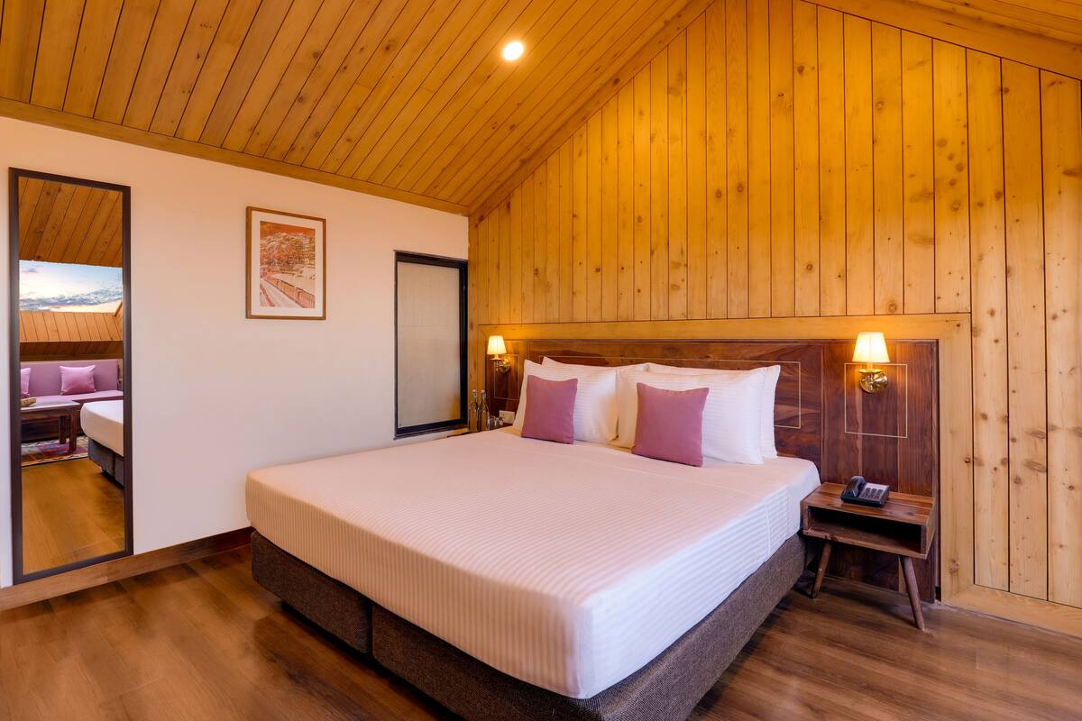 Una cama grande con cabecera de madera, una mesita de noche con lámpara y un cuadro enmarcado en la pared.