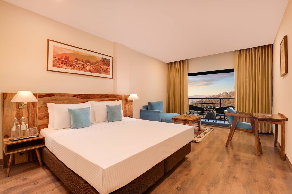 Habitación de hotel con una cama grande, un escritorio, una silla y vistas a la ciudad a través de una ventana.