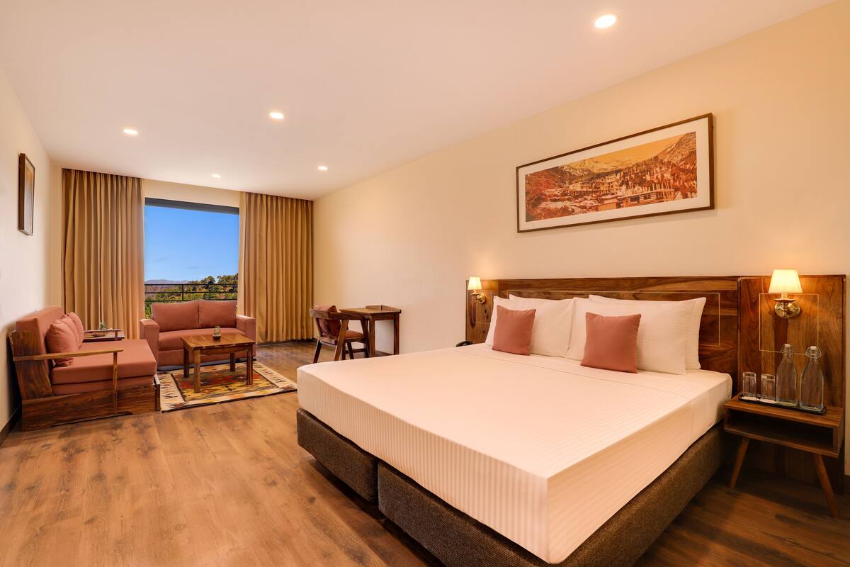 Habitación de hotel con una cama grande, un sofá, una mesita y vistas al exterior.