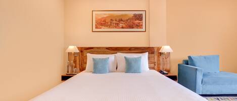 A hotel room with a large bed, two bedside tables with lamps, a blue sofa, and a framed picture on the wall.