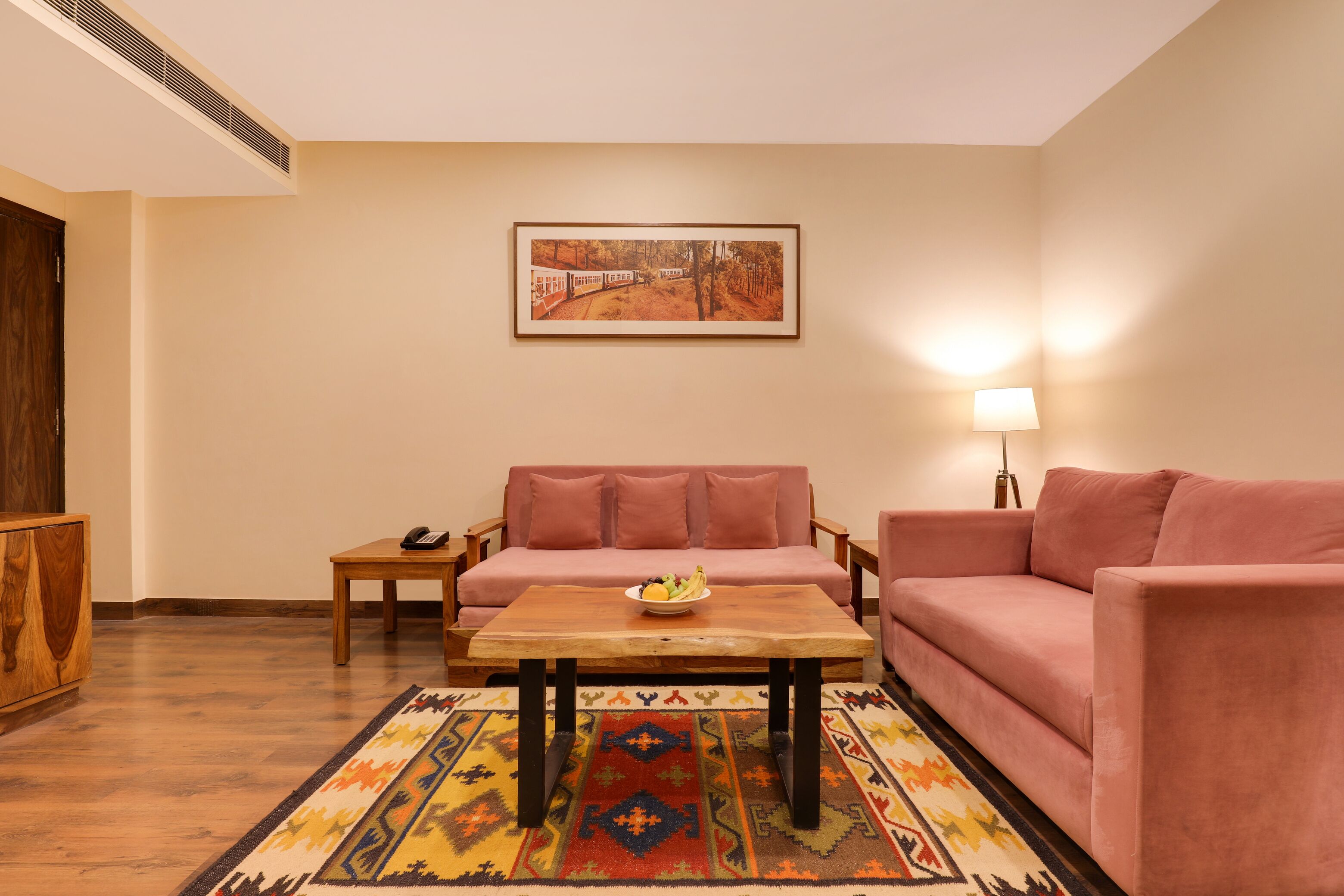 Una sala de estar con un sofá, una mesa de centro, una alfombra, un cuadro en la pared y una lámpara.