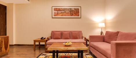 Una sala de estar con un sofá, una mesa de centro, una alfombra, un cuadro en la pared y una lámpara.