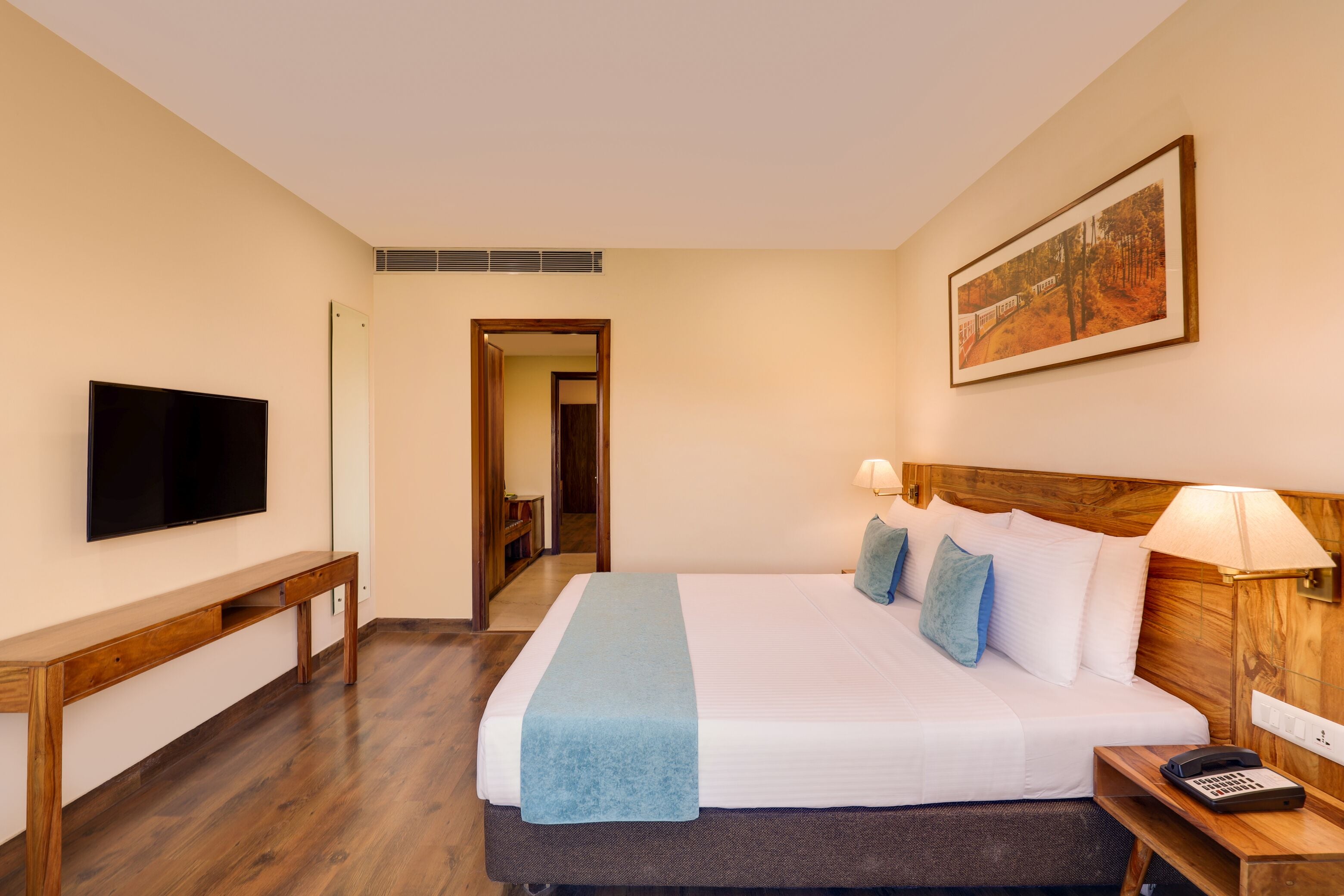 A hotel room with a bed, a TV, a desk, and a painting on the wall.