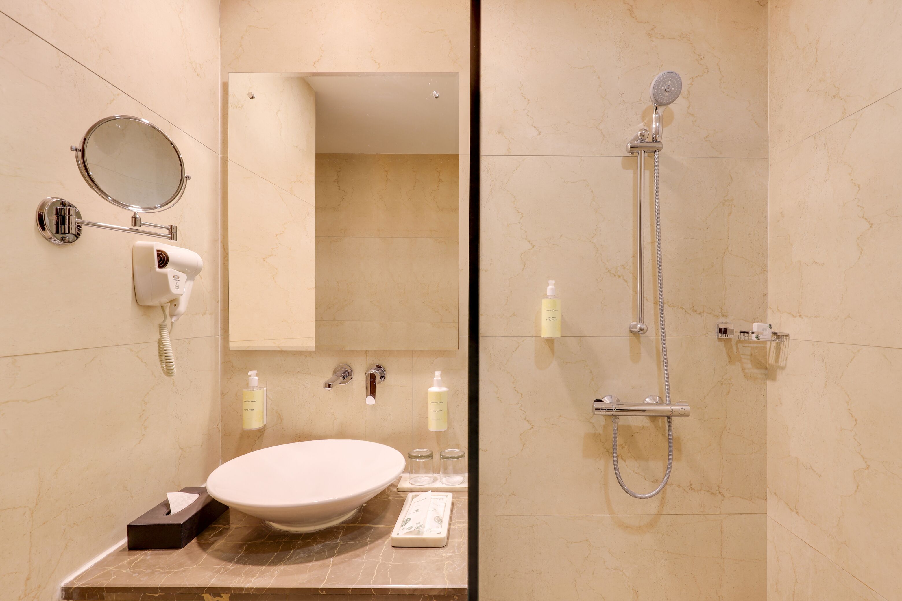 A bathroom with a large oval sink, a handheld mirror, a hairdryer, and a shower with a handheld showerhead.