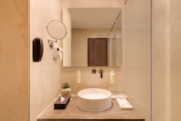Un baño moderno con un lavabo redondo, un espejo, un secador de pelo y artículos de aseo.