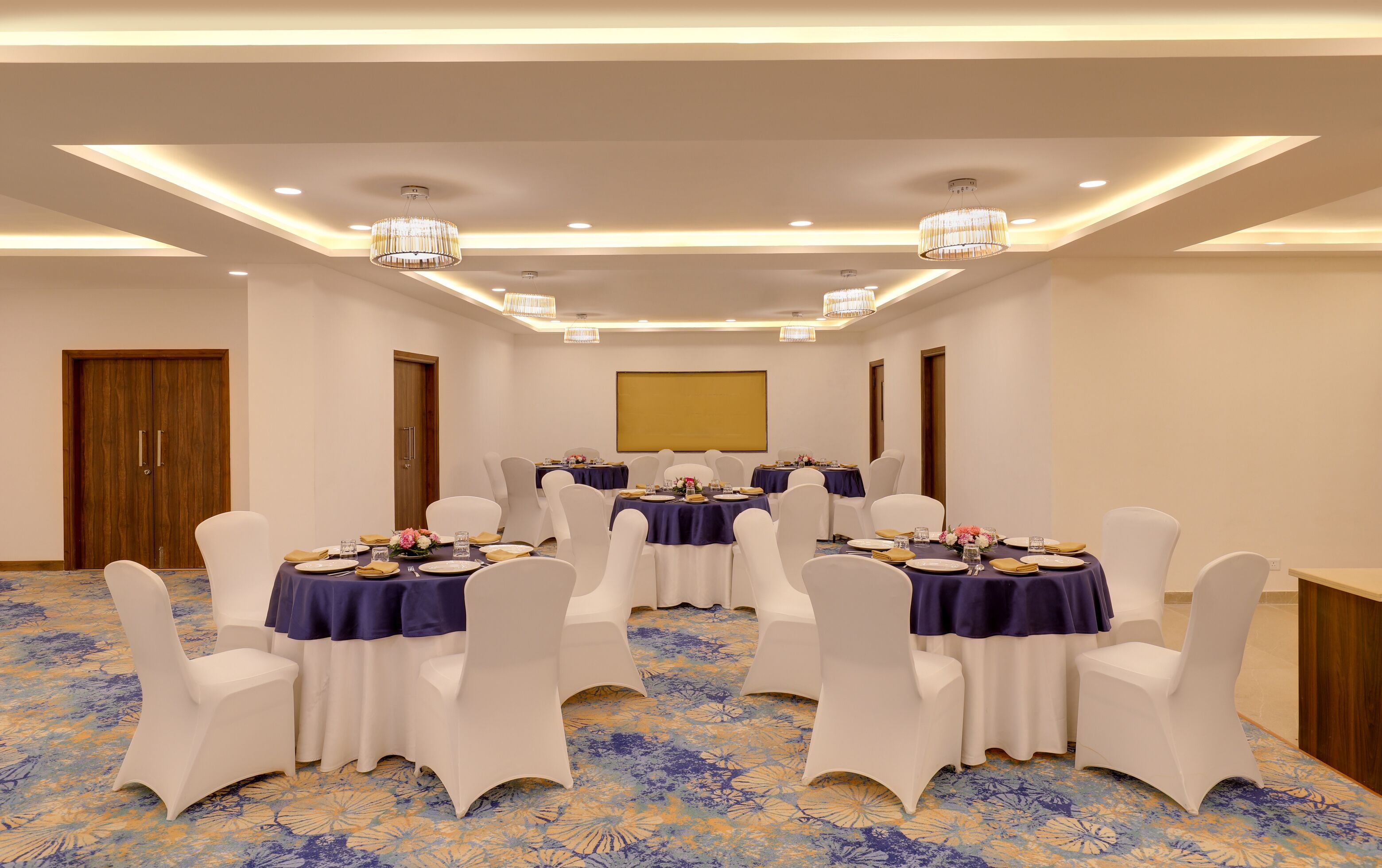 Un salón de conferencias con mesas redondas, sillas blancas y suelo alfombrado.