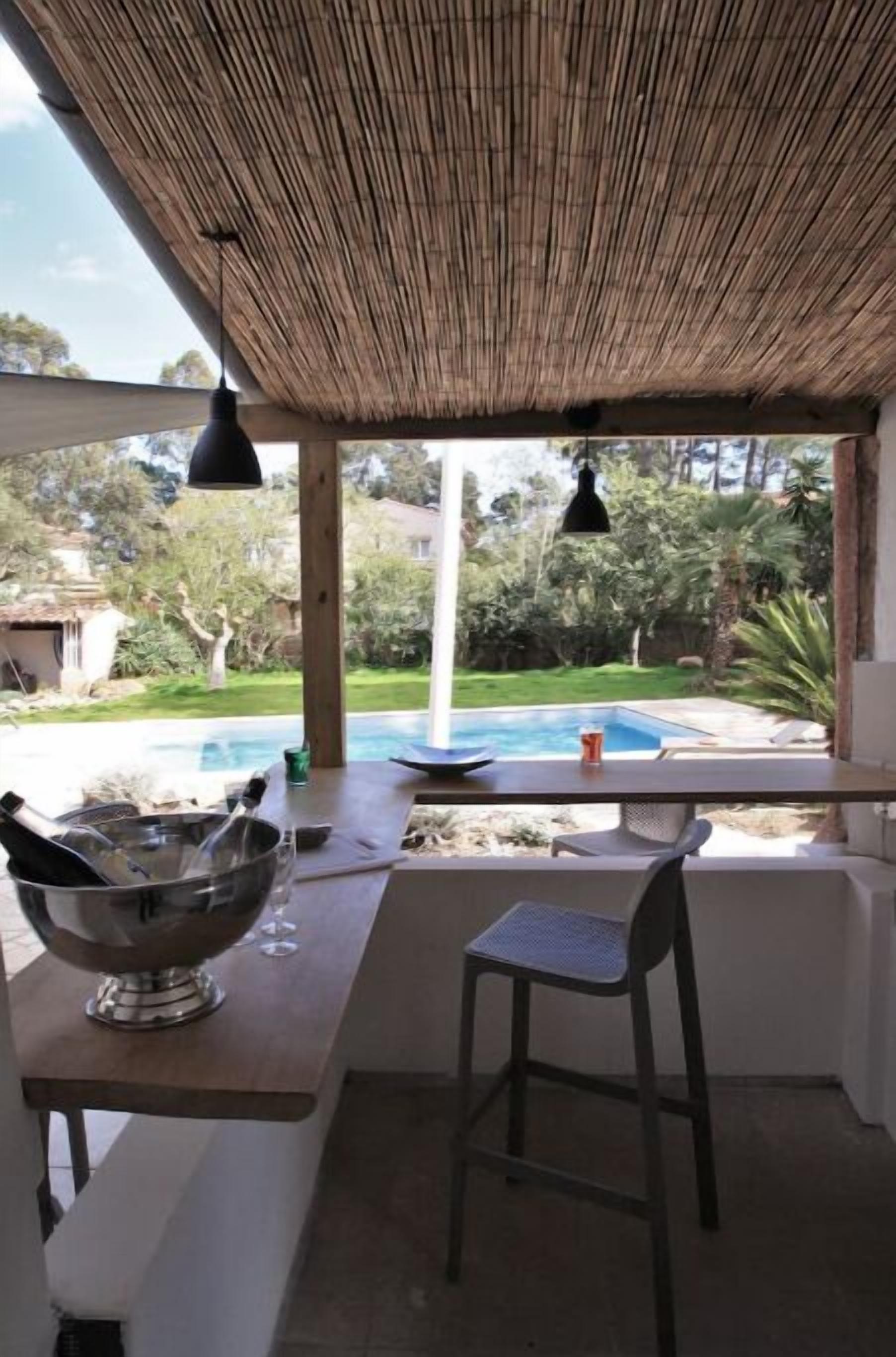A covered outdoor area with a pool, a bar with a metal bowl and bottles, and a chair.