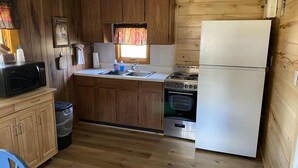 Eine kleine Küche mit Holzausstattung, einer Mikrowelle, einem Spülbecken, einem Herd und einem Kühlschrank.