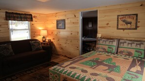 Ein gemütliches Blockhaus-Zimmer mit einer Holzwand, einem Bett mit einer Decke im Elch-Design, einem Holztisch und einer Lampe.