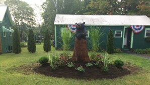 Eine Holzstatue eines Bären auf einem Baumstumpf, umgeben von einem Garten mit verschiedenen Pflanzen und Blumen.