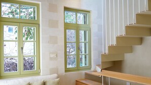 A modern living room with a wooden staircase, a sofa with cushions, and large windows with green frames.