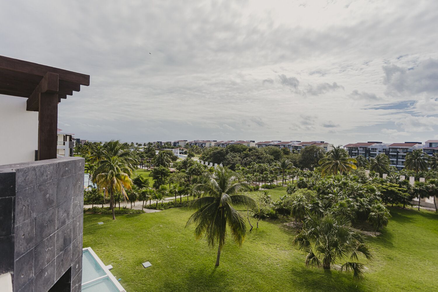 Vue d’un complexe hôtelier avec une piscine, des palmiers et un ciel nuageux.