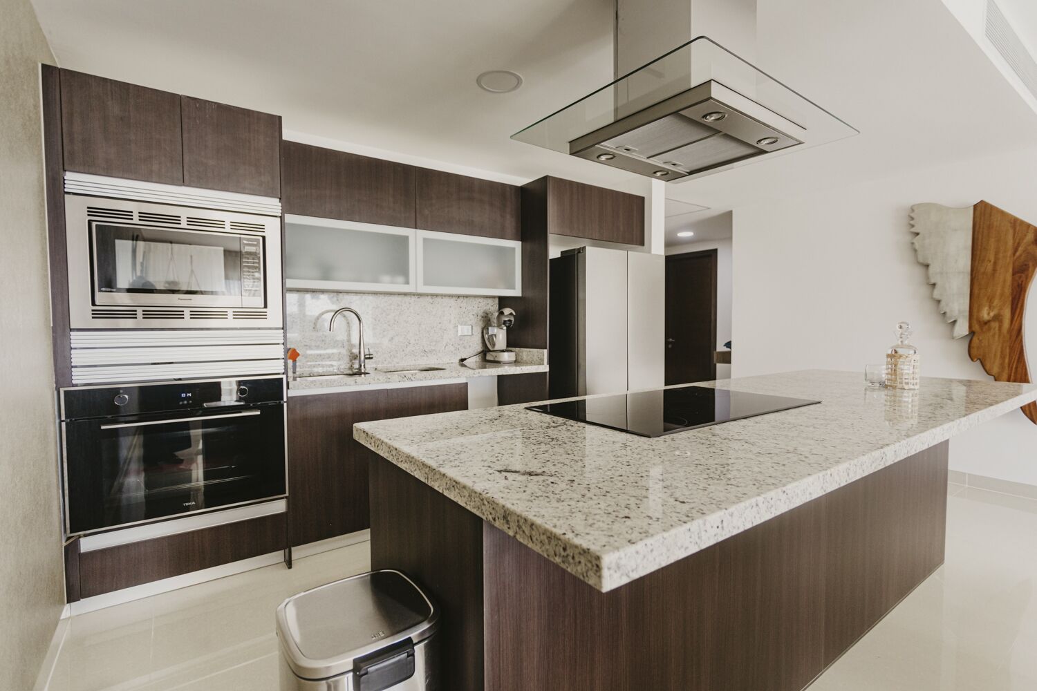 A modern kitchen with dark wood cabinets, a stainless steel oven, a built-in microwave, a granite countertop, and a glass backsplash.