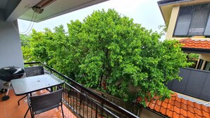 Un balcon avec une table et des chaises, un barbecue et une vue sur un arbre et les bâtiments voisins.