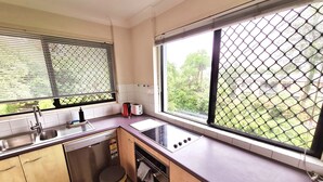 Une cuisine compacte équipée d’un évier, d’une cuisinière et d’une fenêtre donnant sur un espace verdoyant.