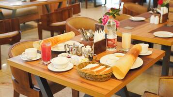 A dining table set with plates, cups, a basket of bread, a bottle of water, and a glass of juice.