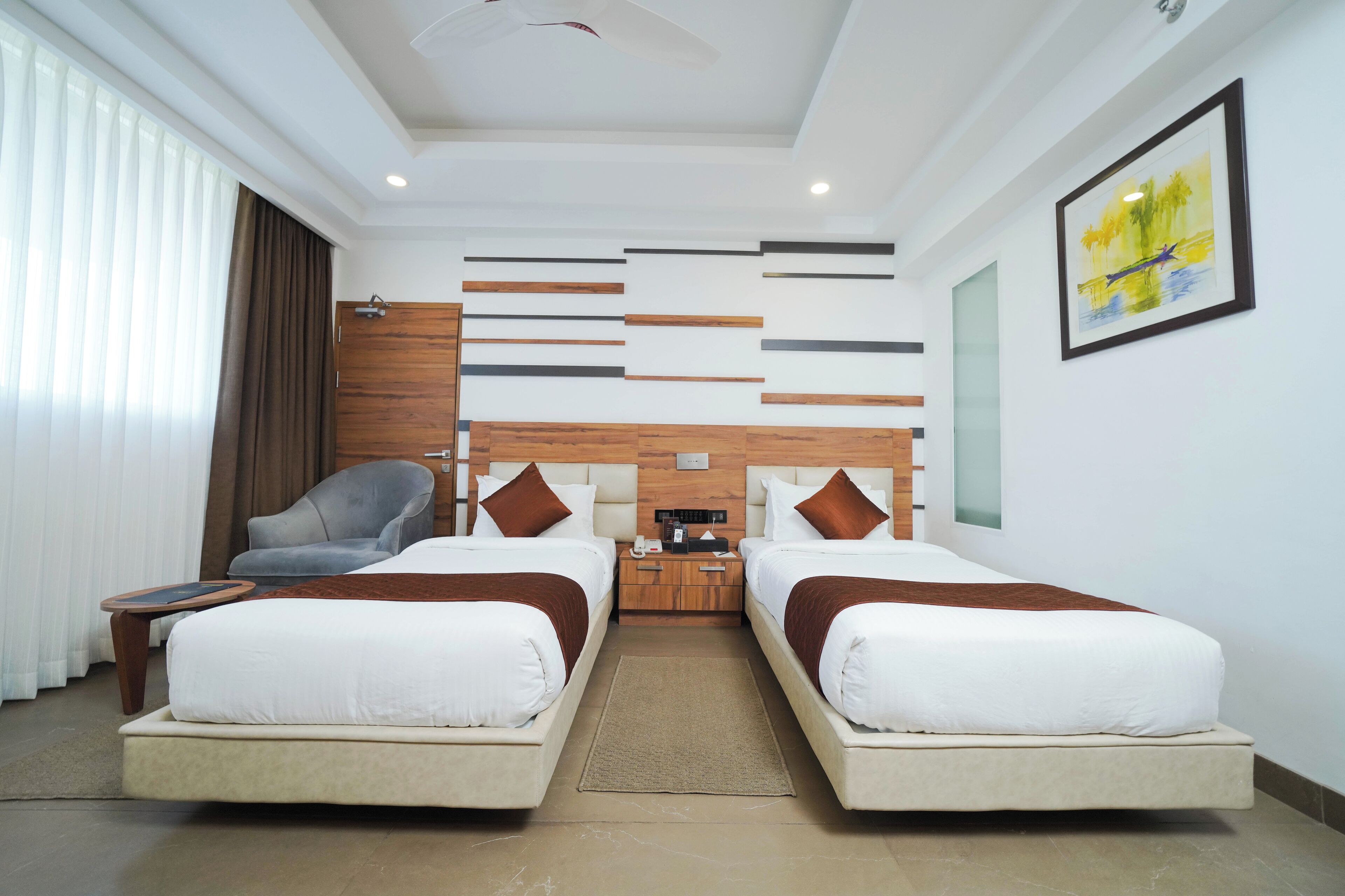 A hotel room with two beds, a desk, a chair, a nightstand, and a painting on the wall.